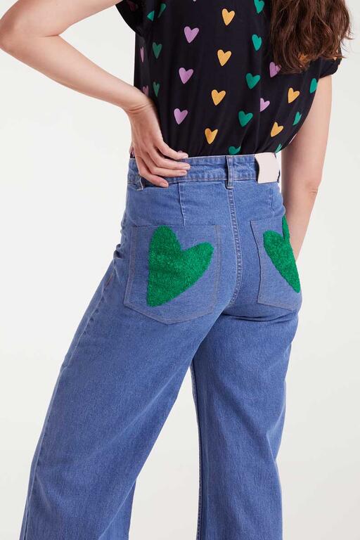 Detalle del bordado de corazones verdes en bolsillos traseros de pantalón vaquero negro de Compañía Fantástica