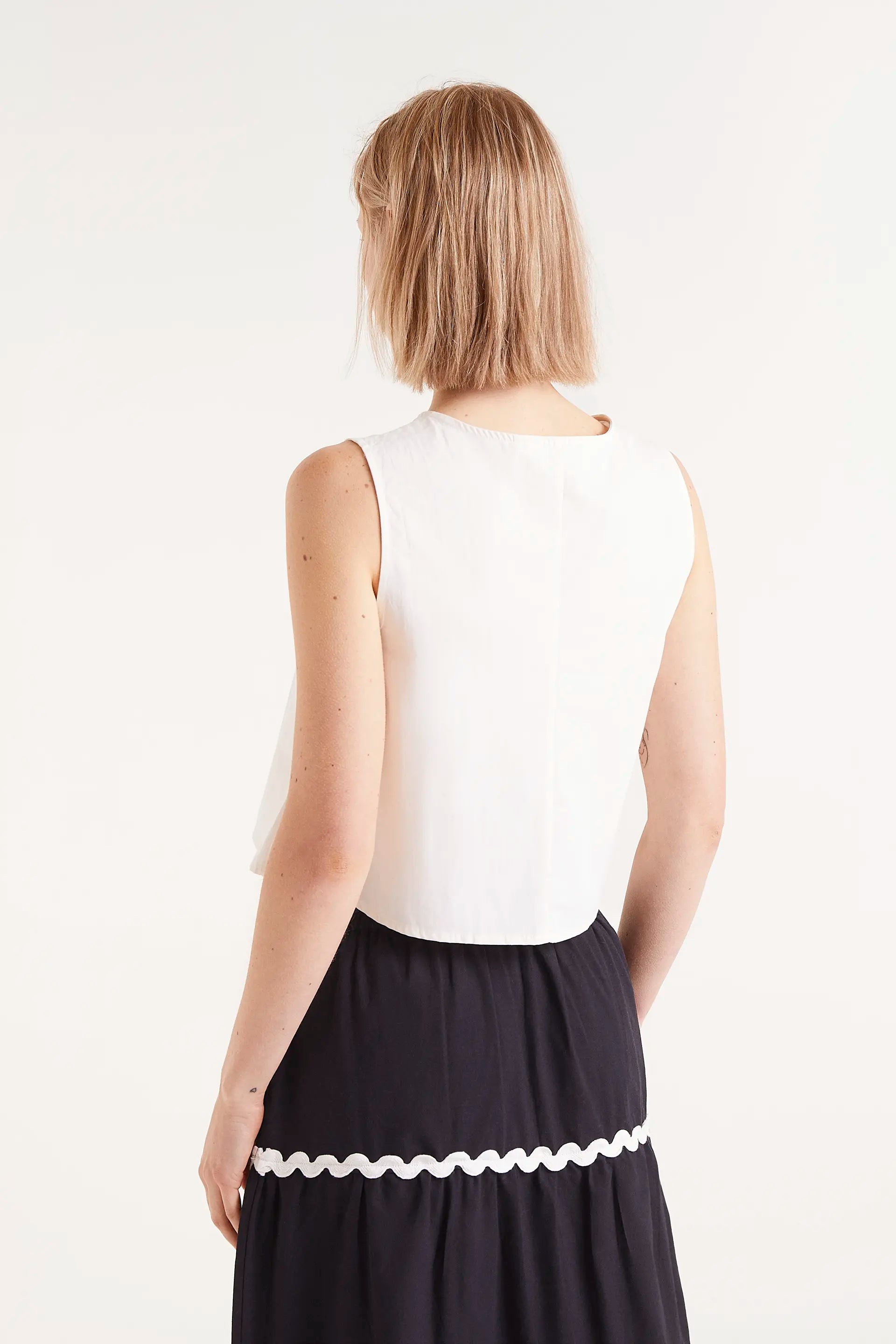Top Sin Mangas Con Botones Blanco. Top blanco sin mangas con botones negros en la parte frontal.