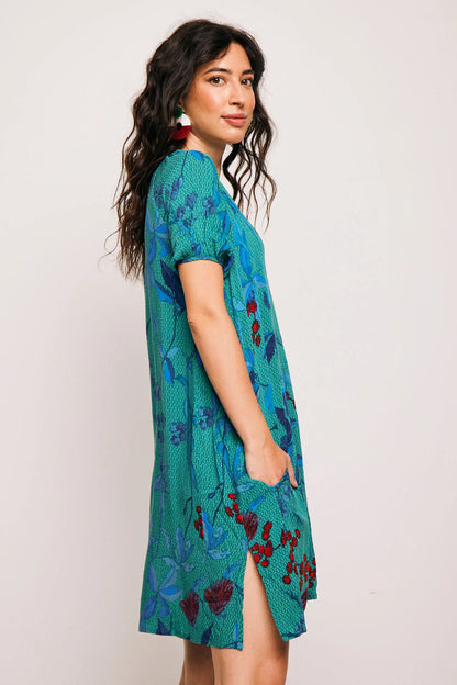 Vestido Famara Smile corto de algodón con estampado tropical en tonos verdes y rojos. Diseño amplio con escote en V y manga corta, ideal para verano.